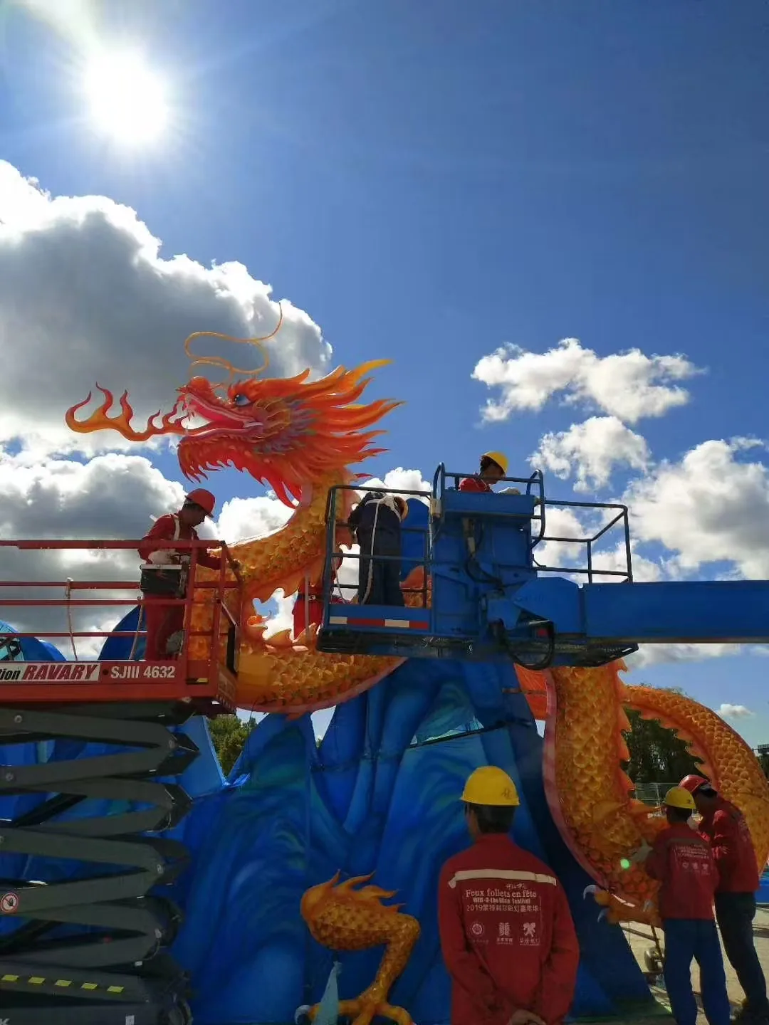 Installation crew positioning a large dragon lantern with mobile lifts